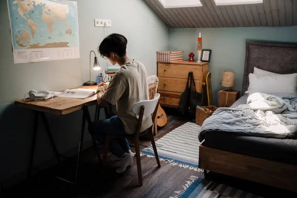 Serious Asian Teenage Guy Studying Book While Sitting Desk Home — Stok fotoğraf