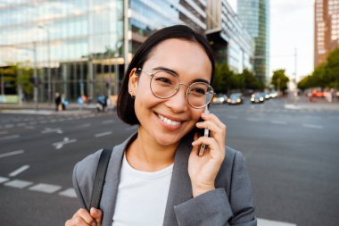 Young asian woman smiling and talking on cellphone while standing at the city street