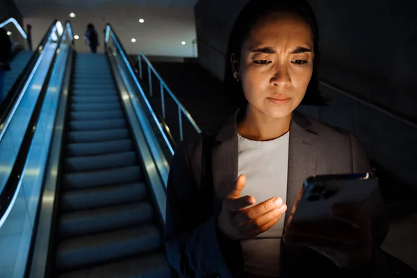 Genç Asyalı Kadın Içeride Yürüyen Merdivende Akıllı Telefon Kullanırken Kaşlarını — Stok fotoğraf