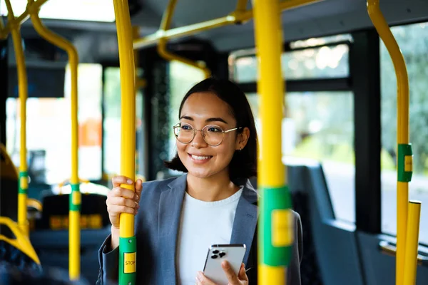 Young Joyful Asian Woman Eyeglasses Holding Smartphone While Traveling Bus — Stockfoto