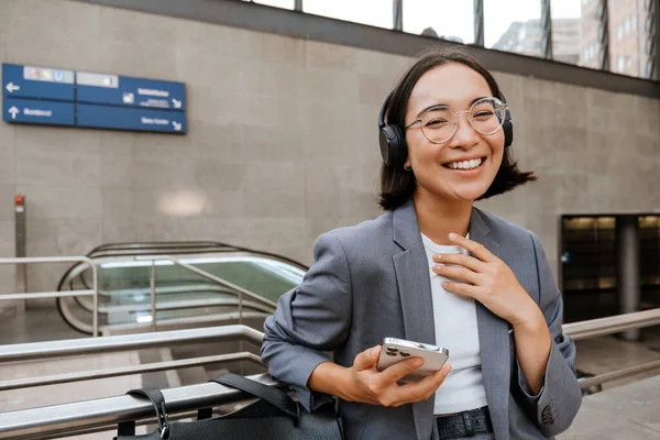 Young Cheerful Asian Woman Headphones Wearing Suit Using Mobile Phone — Stok fotoğraf