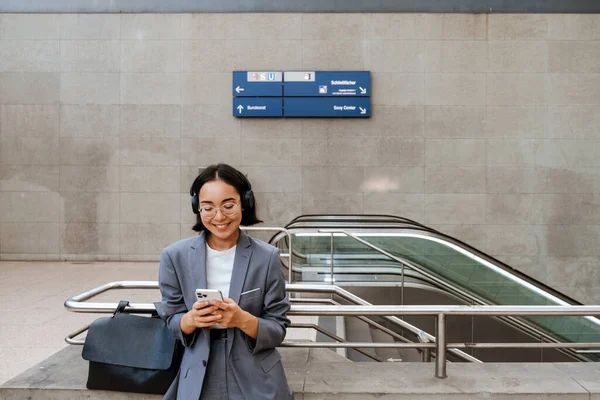 站在自动扶梯附近时 手持智能手机的年轻笑脸亚洲女人 — 图库照片