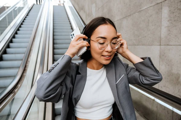 Gözlüklü Güzel Asyalı Kadın Yürüyen Merdivende Dururken Kulaklık Takıyor — Stok fotoğraf