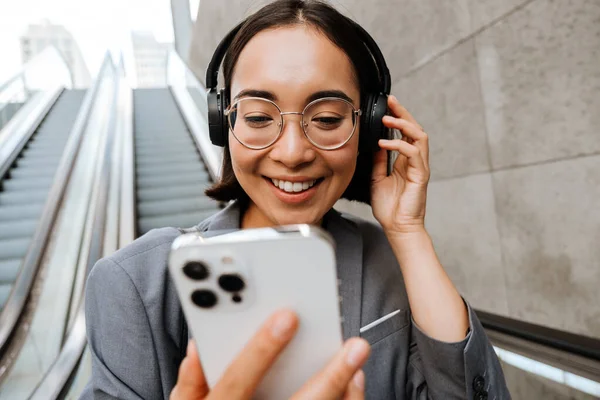 Jovem Sorrindo Mulher Asiática Fones Ouvido Usando Telefone Celular Enquanto — Fotografia de Stock