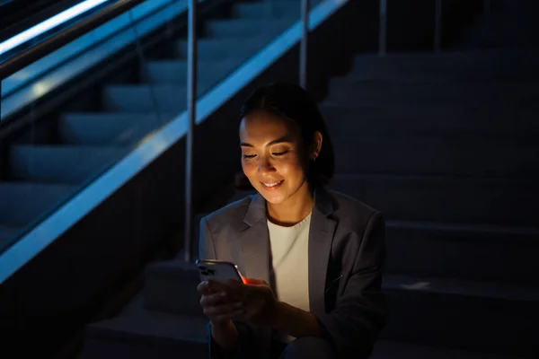 Joven Sonriente Mujer Asiática Vistiendo Traje Usando Teléfono Móvil Mientras —  Fotos de Stock