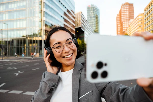 Young Joyful Asian Woman Headphones Taking Selfie Smartphone While Standing — Stockfoto