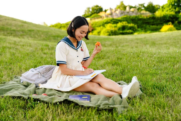 Young Smiling Asian Woman Wearing Dress Writing Notes Eating Fruits — Stockfoto