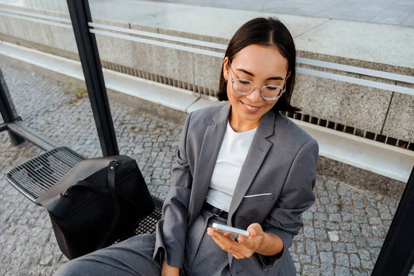 Young Asian Woman Glasses Smiling Using Mobile Phone While Sitting — Stockfoto