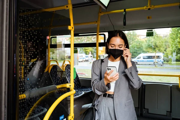 Młoda Azjatka Masce Medycznej Stojąca Publicznym Autobusie Smartfonem Rękach — Zdjęcie stockowe