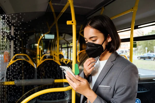 Młoda Azjatka Masce Medycznej Stojąca Publicznym Autobusie Smartfonem Rękach — Zdjęcie stockowe