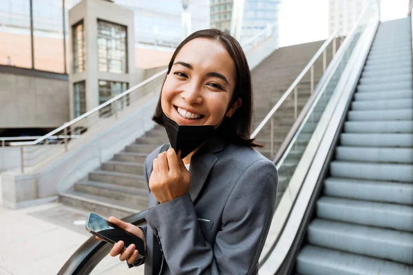 Mladá Usměvavá Asijská Žena Lékařské Masce Drží Mobilní Telefon Zatímco — Stock fotografie
