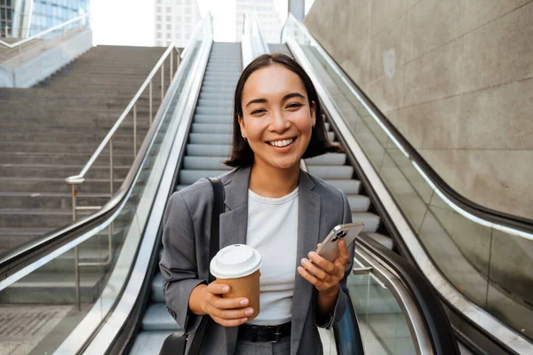 Joven Mujer Asiática Sonriendo Cámara Sosteniendo Teléfono Móvil Café Mientras — Foto de Stock