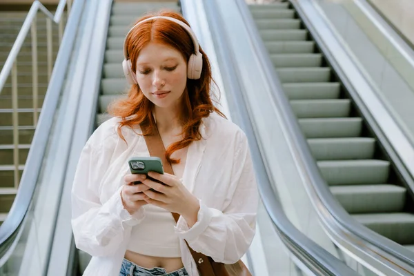Young White Woman Wearing Headphones Using Mobile Phone While Standing — Stok fotoğraf