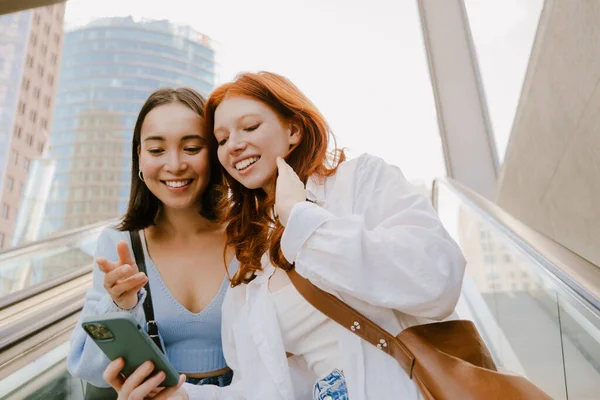 Mladé Nadnárodní Ženy Usmívají Používají Mobilní Telefon Když Stojí Eskalátoru — Stock fotografie
