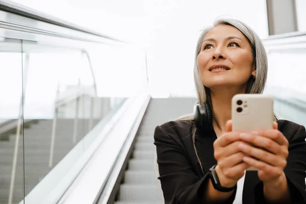 在室内扶梯上使用手机的成熟亚洲女人 — 图库照片