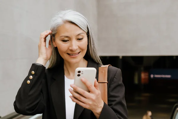 Grey Asian Woman Smiling Using Mobile Phone While Standing Escalator — Zdjęcie stockowe