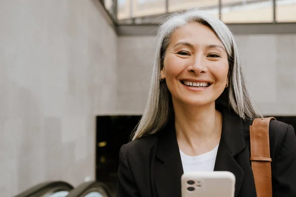 Mujer Asiática Gris Sonriendo Usando Teléfono Móvil Mientras Está Pie —  Fotos de Stock