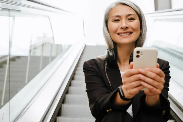 Starší Asijské Žena Pomocí Mobilního Telefonu Při Sezení Eskalátoru Uvnitř — Stock fotografie
