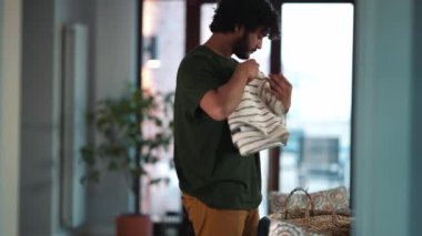 Concentrated curly haired Indian man stacking things after washing at home
