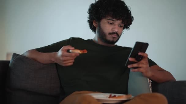 Bonito Cabelo Encaracolado Indiano Homem Digitando Celular Comer Pizza Enquanto — Vídeo de Stock
