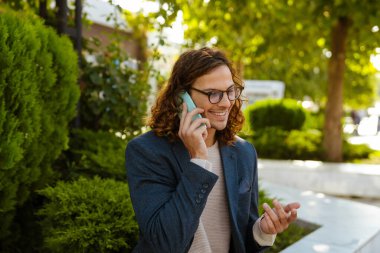 Ginger european man talking on mobile phone while sitting in summer park