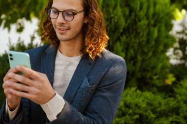 Ginger european man talking on mobile phone while sitting in summer park