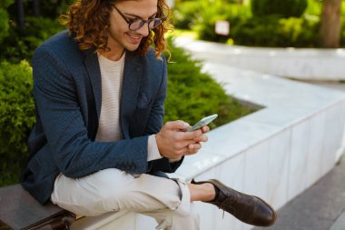 Ginger european man talking on mobile phone while sitting in summer park