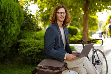 Ginger european man working with laptop while sitting in summer park
