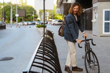 Ginger european man wearing jacket walking with bicycle on city street