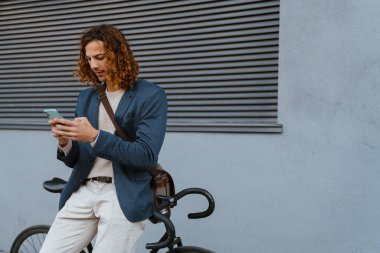 Ginger european man using mobile phone while sitting on bicycle at city street
