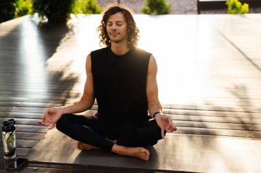 Young ginger man gesturing and meditating during yoga practice outdoors