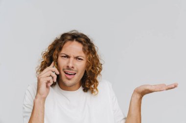 Ginger european man expressing outrage while talking on cellphone isolated over white background