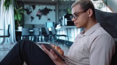 Cute man with piercing and dyed blond hair working on tablet in the office