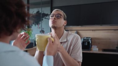 Handsome man with piercing and dyed blond hair talking about work with brunette woman in the office