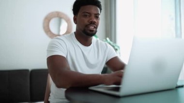 Pretty African man typing on laptop while sitting at home