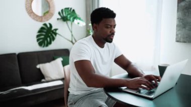 Concentrated African man typing on laptop while sitting at home