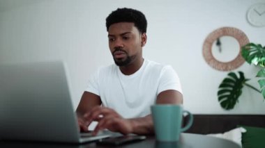 Positive African man talking by video call on laptop while sitting at home