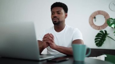 Concentrated African man talking by video call on laptop while sitting at home