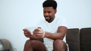 Cheerful African man wearing white t-shirt playing video game on mobile and rejoicing about victory at home
