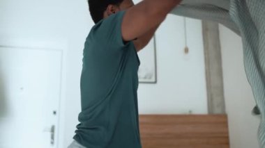 Pretty African brunet man makes his bed in the morning at home