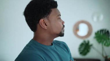 Pensive African brunet man wearing blue t-shirt thinking about something at home