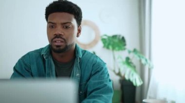 Concentrated African brunet man working on laptop while sitting in the room at home