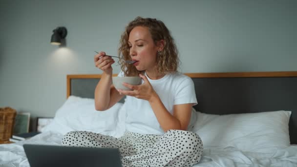 Curly Haired Positive Woman Eating Cereal Milk Watching Movie Laptop — Vídeo de stock
