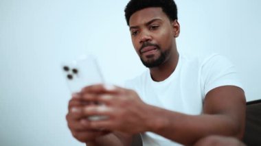 Concentrated African brunet man texting on phone while sitting at home