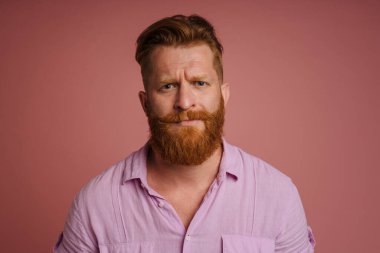 Ginger white man with beard frowning and looking at camera isolated over pink background
