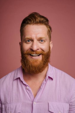 Ginger white man with beard smiling and looking at camera isolated over pink background