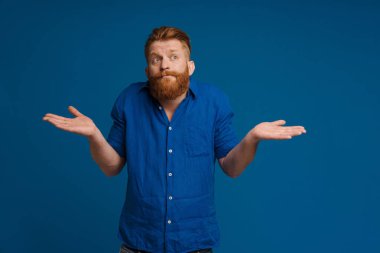 Ginger white man with beard looking at camera and holding copyspace isolated over blue background