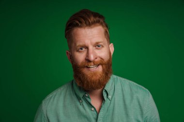 Ginger white man with beard smiling and looking at camera isolated over green background