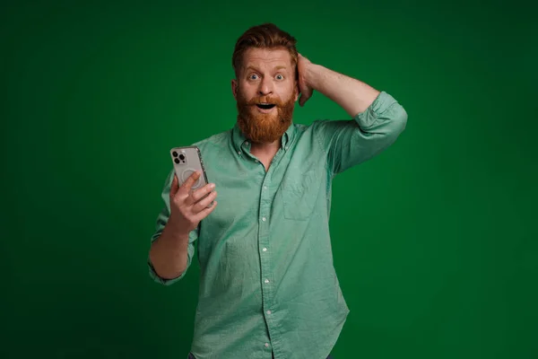 Ginger White Man Expressing Surprise Using Mobile Phone Isolated Green — 图库照片