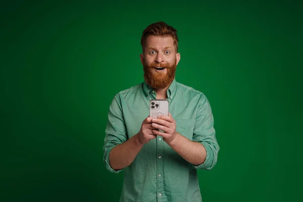 Ginger White Man Expressing Surprise Using Mobile Phone Isolated Green — Stockfoto
